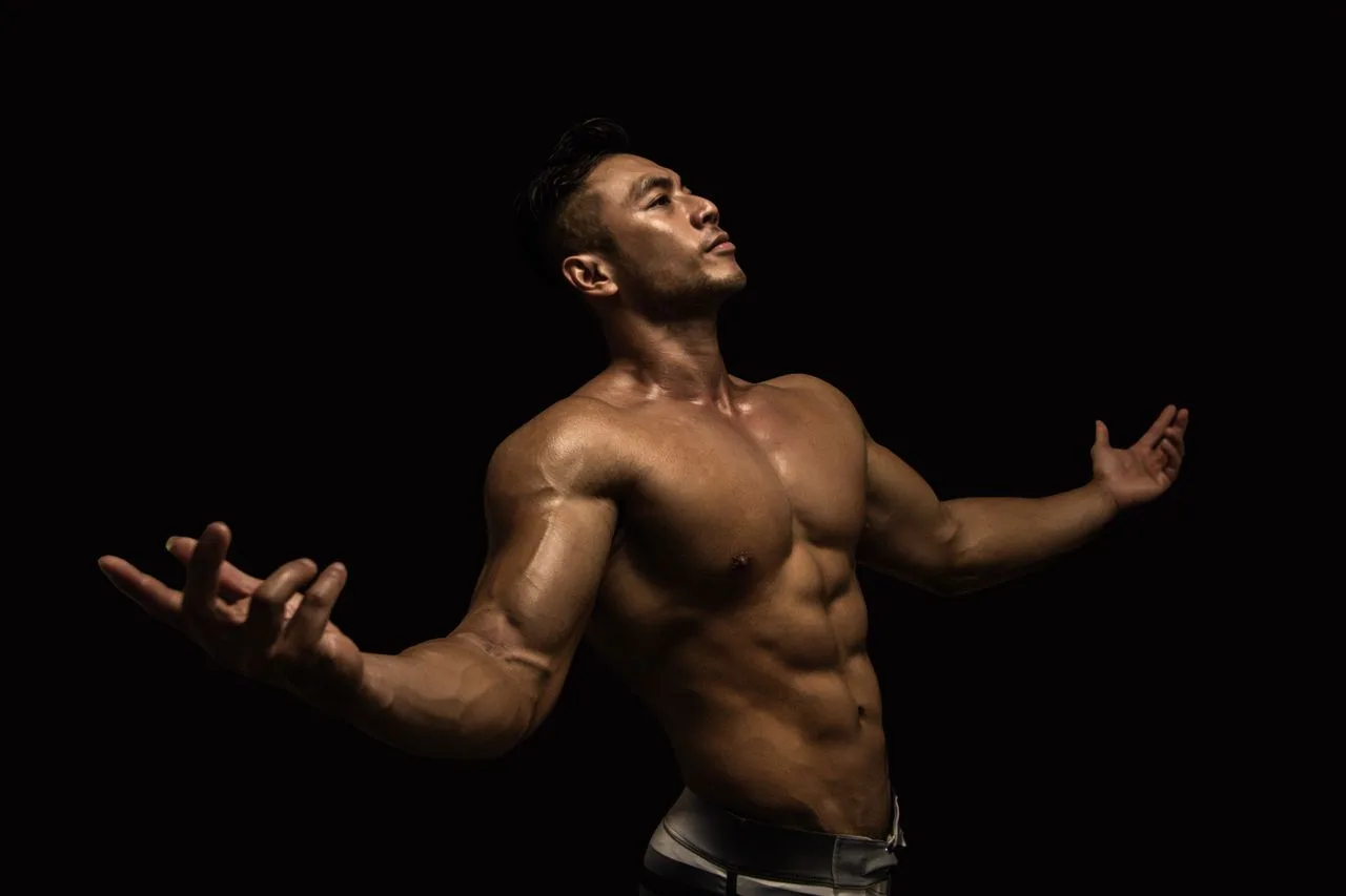 Muscular male model posing confidently in a dramatic lighting environment, showcasing fitness and strength.